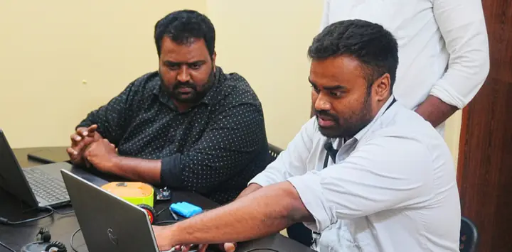 A trainer coaching a teacher on a laptop with a robotics kit